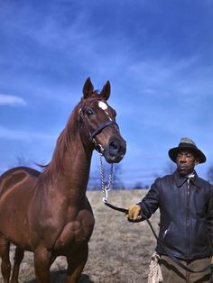 a man standing next to a brown horse on top of a dry grass covered field