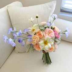 a bouquet of flowers sitting on top of a white couch next to a blue window