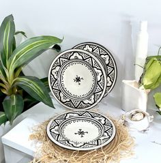 two black and white plates sitting next to each other on a table with plants in the background