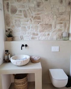 a white toilet sitting next to a bathroom sink under a stone wall mounted above it