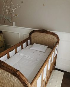 a baby crib with white linens and pillows on the bottom row, in front of a beige wall