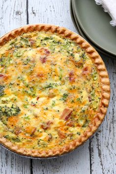 a quiche with broccoli, cheese and bacon in a pie pan on a wooden table