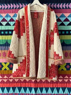 a colorful quilted jacket hanging on a wall next to a white coat with red trim