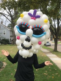 a woman in a black dress is wearing a large balloon skull mask on her head