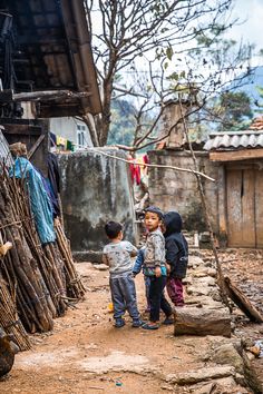 two small children standing next to each other in front of a shack with clothes hanging on the line