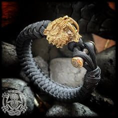 a black and gold bracelet with a lion head on it's end, sitting next to some rocks