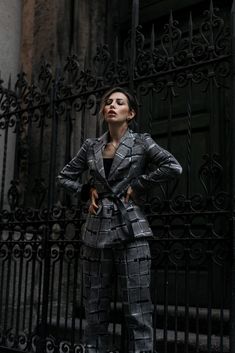 a woman standing in front of an iron gate wearing a suit and heels with her hands on her hips