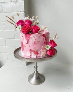 a pink cake decorated with flowers on top of a metal stand in front of a brick wall