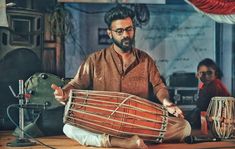 a man sitting on the floor playing an instrument with two other people in the background