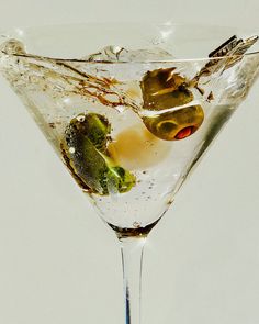 a martini with olives and ice on the rim is shown in this artistic photograph