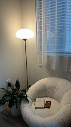 a white chair sitting in front of a window next to a potted plant and lamp