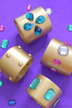 three gold rings with blue and green stones on purple surface next to other jewelry items