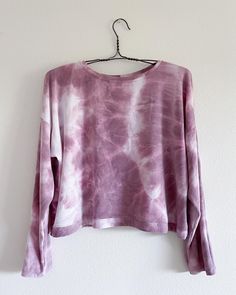 a pink and white tie - dyed sweater hanging on a hanger against a wall