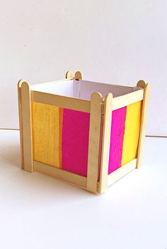 a wooden box with pink, yellow and orange squares on the inside is sitting on a white surface