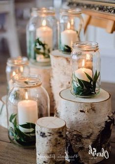 some candles are sitting in glass jars with greenery on the top and one candle is lit