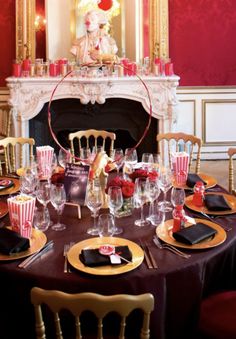 a table set with wine glasses, plates and napkins in front of a fire place