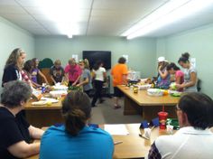 a group of people standing around a room with food on the table and in front of them