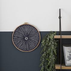 a black and white striped wall with a wooden shelf holding two framed pictures, a potted plant and a wicker wheel hanging on the wall