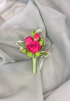 a single pink rose is sitting on a white cloth with green stems and leaves in the center