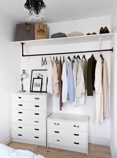 a white closet with clothes hanging on the wall and drawers below it, along with a chandelier