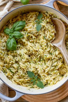 a large pot filled with rice and basil on top of a wooden table next to a spoon