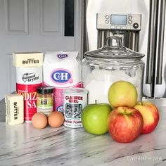 apples, flour, butter, eggs and other ingredients on a counter top in front of an appliance