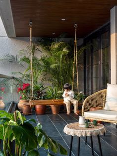 a person sitting on a porch swing in front of some plants and potted plants