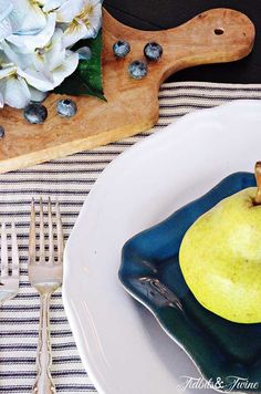 a plate with an apple on it next to a knife and fork, near a cutting board