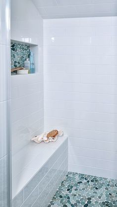 a white tiled bathroom with blue and green tiles on the shower wall next to it