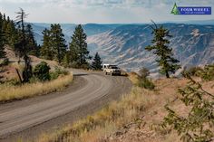 a van is driving down a dirt road in the middle of some trees and mountains