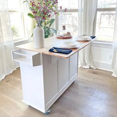 a kitchen island with plates on it in front of two windows and flowers behind the counter