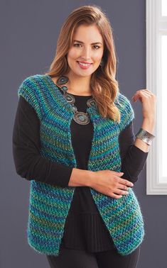 a woman standing in front of a window wearing a blue and green knitted vest