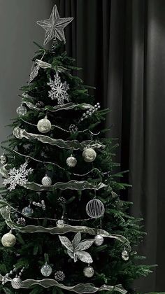 a christmas tree with ornaments on it in front of a black curtained room window