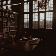 a dark room with lots of books on the shelves and two people sitting at a table in front of them