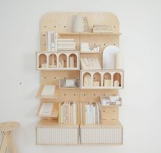 a wooden shelf with books and other items on it next to a small stool in front of a white wall