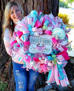 a woman is holding up a wreath that says sweet shop with pink, blue and green ribbons