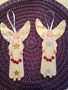 two wooden angel ornaments with red beads on them sitting on top of a purple mat