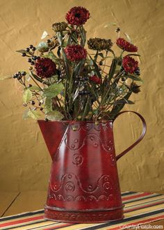 a red vase filled with lots of flowers sitting on top of a striped table cloth