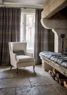 a chair sitting in front of a fire place next to a window with curtains on it