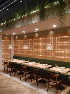 an empty restaurant with wooden tables and green bench seating, hanging plants on the wall