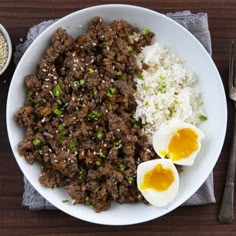 a white plate topped with rice and meat next to an egg on top of it