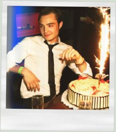 a man cutting into a birthday cake with a lit candle on the table next to it