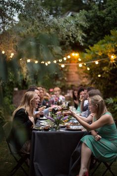 a group of people sitting around a table eating food and drinking wine at an outdoor dinner party