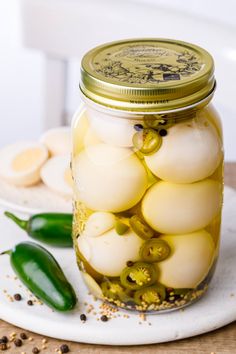 a jar filled with pickles sitting on top of a white plate next to green peppers