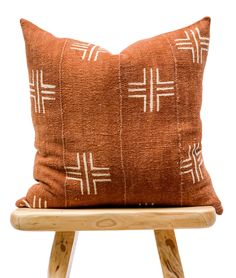 an orange pillow with white crosses on it sitting on a wooden stool in front of a white wall