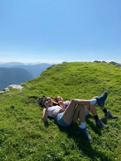 two women laying on the grass in front of mountains