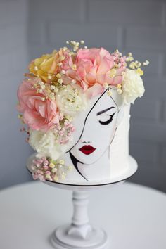 a white cake with flowers on top and a woman's face painted on it