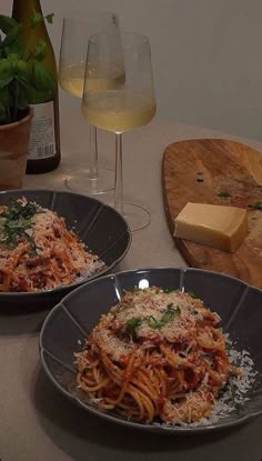 two plates of spaghetti with cheese and parmesan bread on a table next to wine glasses