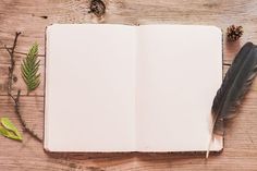 an open notebook with a pen and some leaves on it next to a pine cone