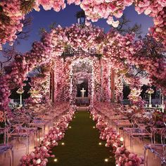 an outdoor wedding setup with pink flowers and candles on the aisle, surrounded by clear chairs